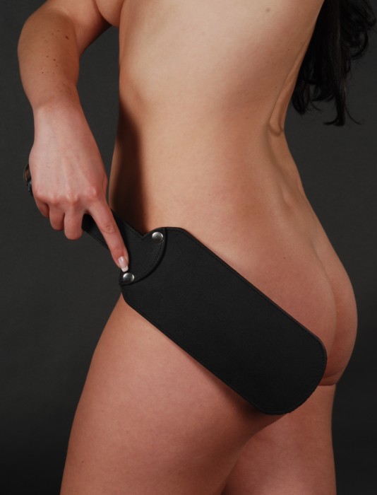 Model mit schwarzem Lederpaddel in der Hand an ihrem Rücken