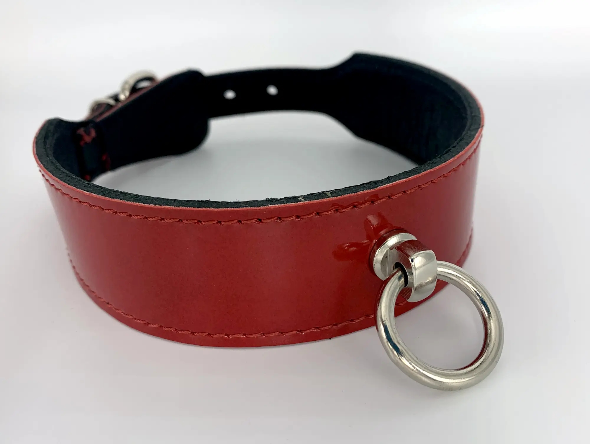 Breites Halsband aus rotem Lackleder mit schwarzem Innenfutter, roter Ziernaht und silbernem O-Ring, schräg von vorne fotografiert auf hellem Untergrund